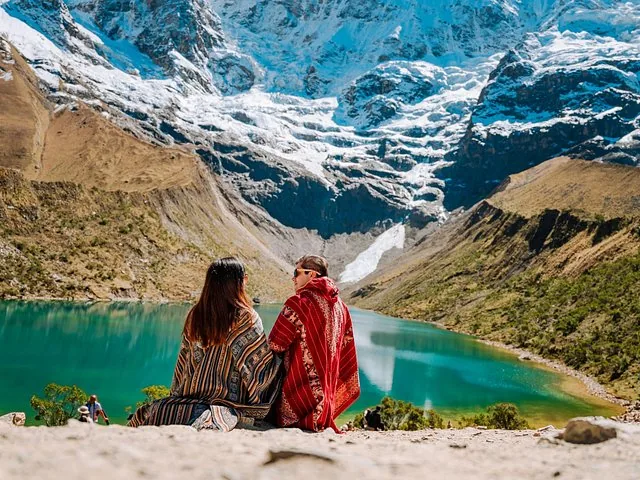 Couple wearing colorful ponchos sitting beside picturesque Humantay Lake