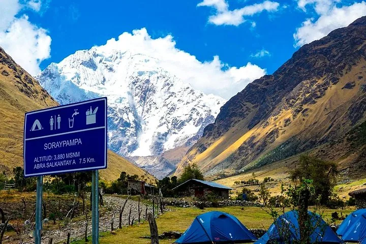 Schild von Soraypampa, blaue Zelte und majestätische Berggipfel im Hintergrund
